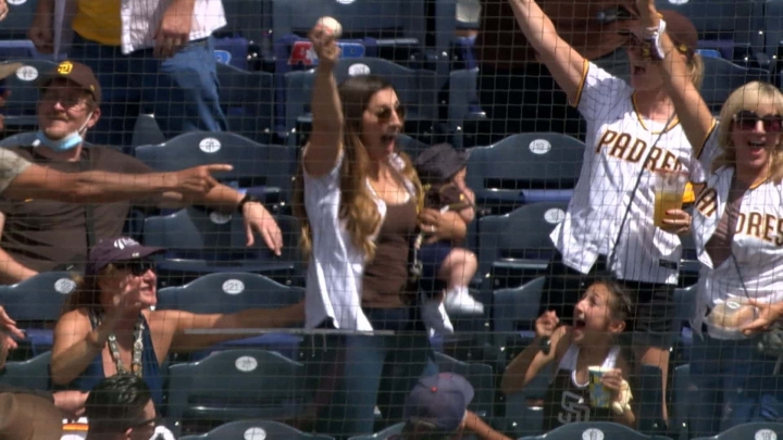 Mujer atrapa una pelota de béisbol con todo y su hijo en brazos.